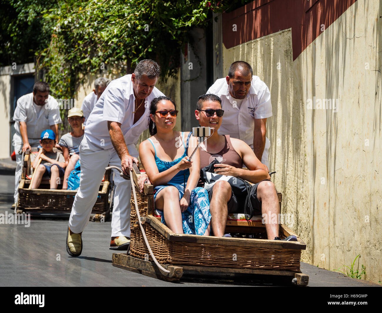 Los conductores de trineo de vestido con ropas blancas tradicionales llevan turistas en un tobogán de madera desde el Monte bajando la colina hacia Funchal. Foto de stock