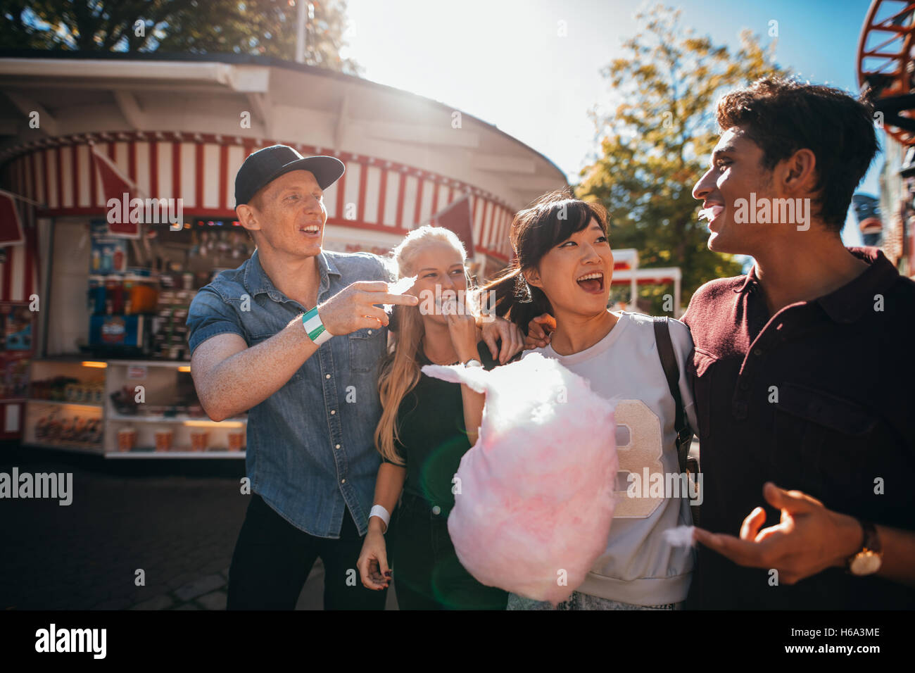 Grupo de Amigos divirtiéndose mientras come algodón de azúcar en el recinto ferial. El hombre y la mujer joven con candyfloss en el parque de diversiones. Foto de stock