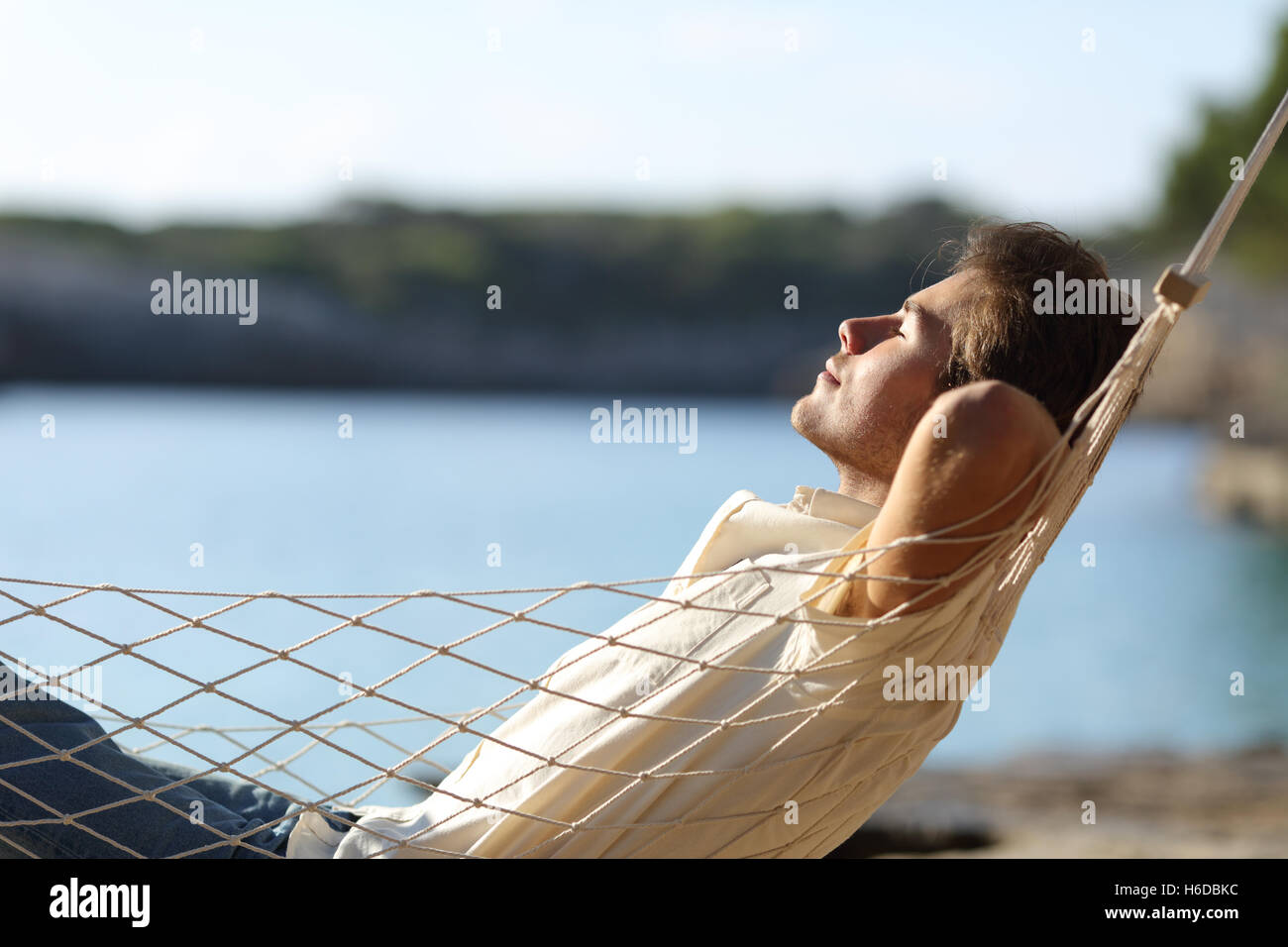 Vista lateral de un hombre feliz casual relajándose en una hamaca en la playa de vacaciones Foto de stock