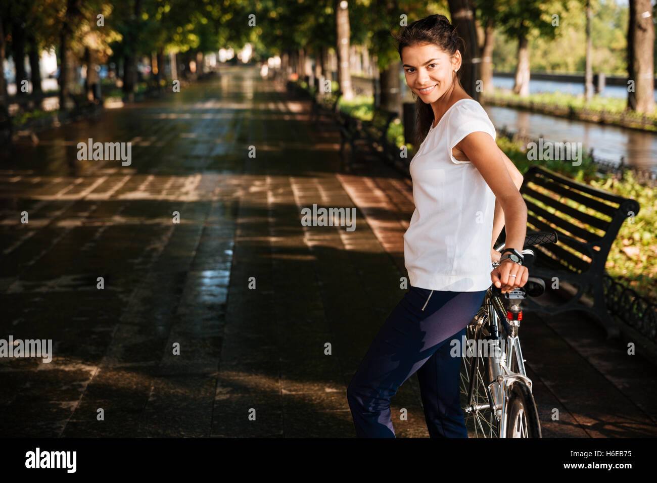 Casual sonriente chica con bicicleta en el parque de la calle Foto de stock