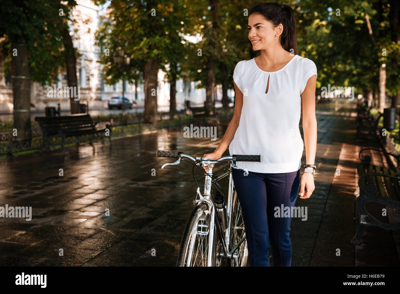 Morena Casual niña sonriente caminando en el parque de la ciudad con bicicleta Foto de stock