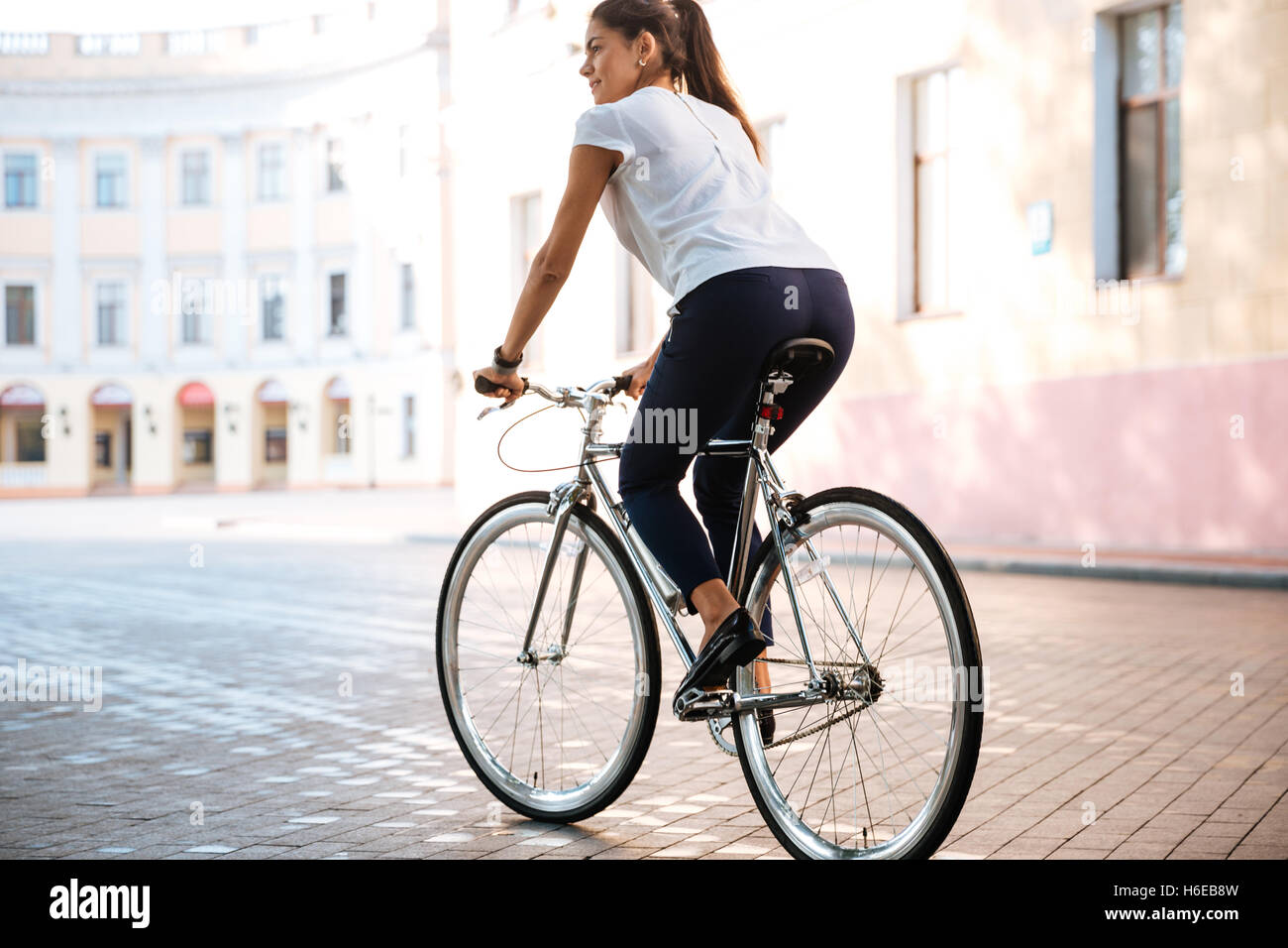 Mujer morena joven montando en bicicleta en las calles de la ciudad Foto de stock