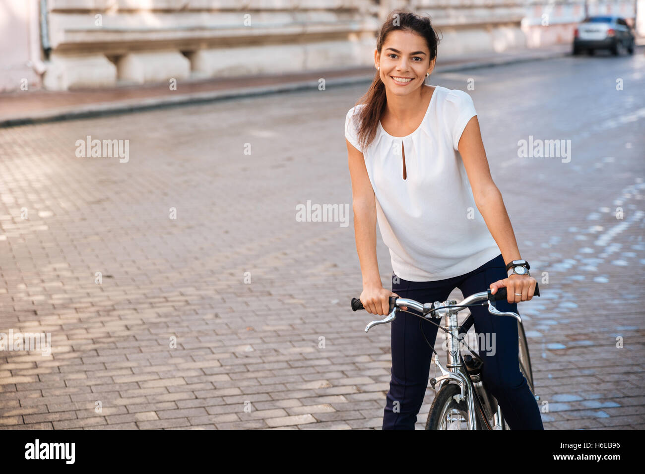 Retrato de una mujer bonita montando en bicicleta en las calles de la ciudad y mirando a la cámara Foto de stock
