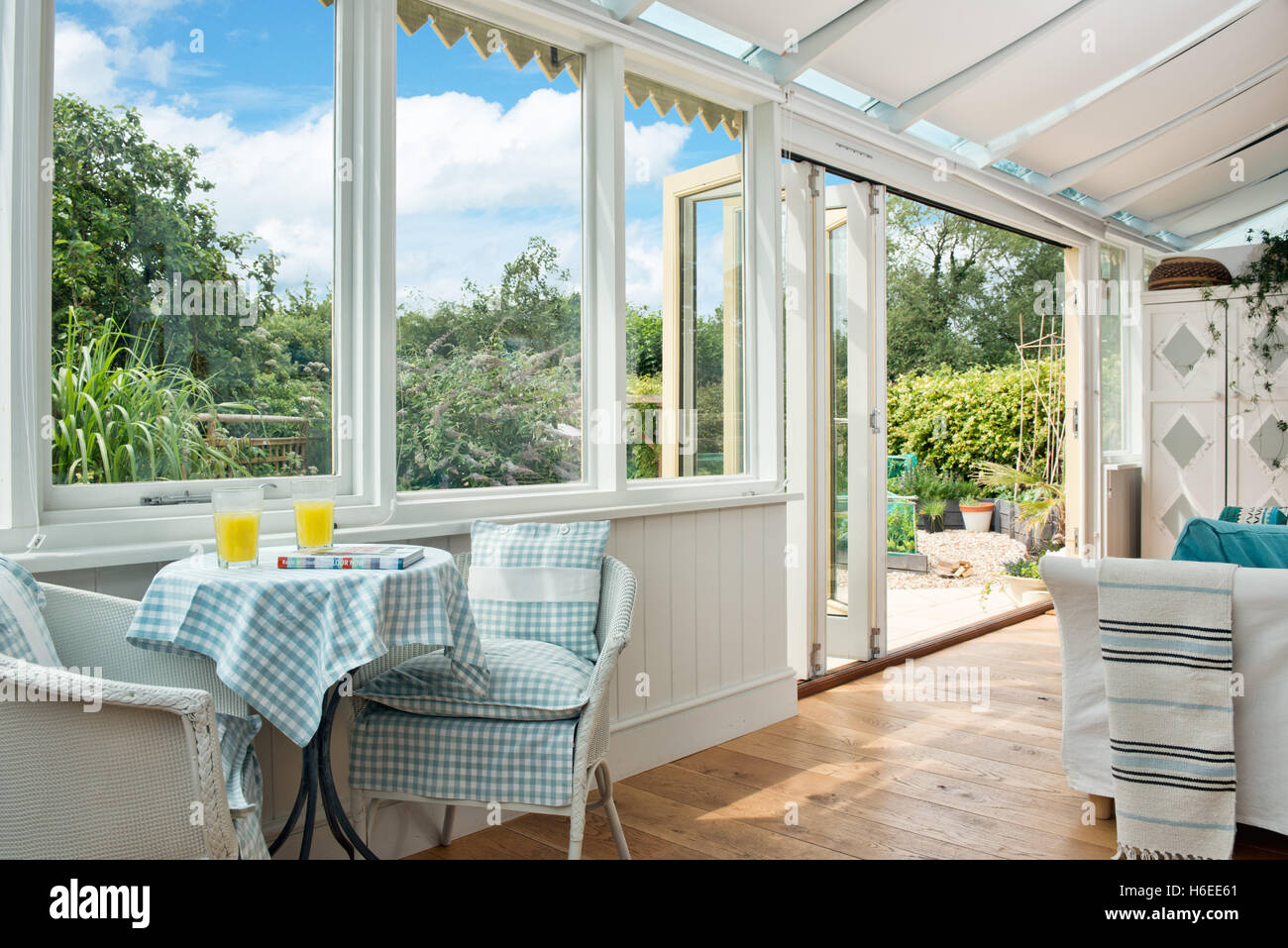 Una mesa puesta para el desayuno con tela de algodón a cuadros, manteles en un conservatorio con grandes puertas abiertas al jardín en un día soleado en el Reino Unido. Foto de stock