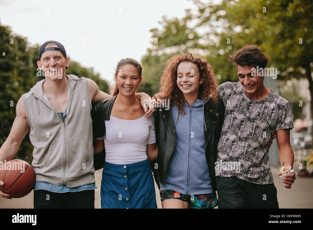 Retrato de grupo multirracial de gente disfrutando de un paseo al aire libre. Cuatro jóvenes amigos caminando juntos y sonrientes en las calles de la ciudad Foto de stock