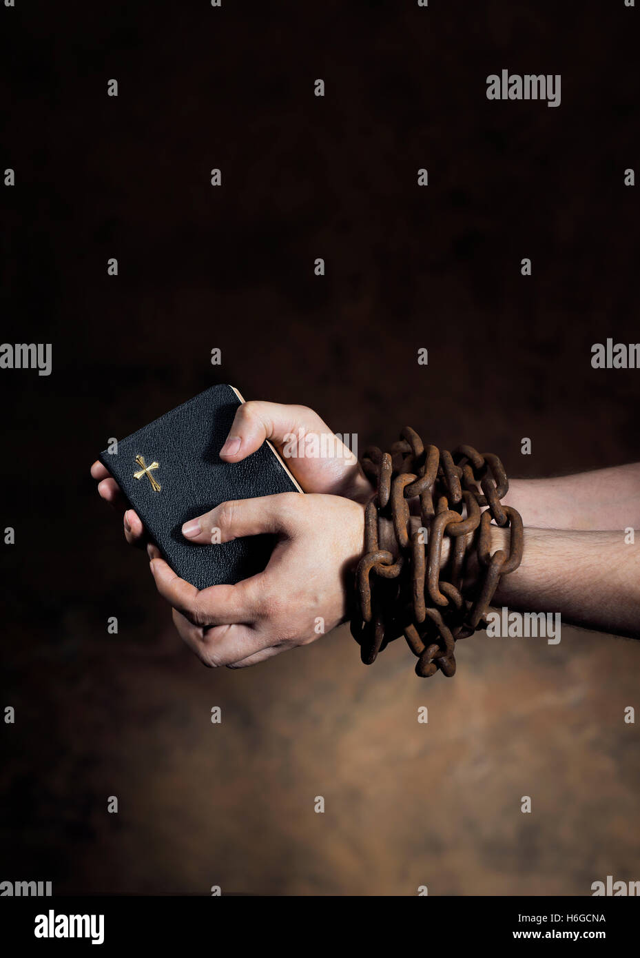 Manos sosteniendo una biblia atados juntos con una vieja cadena oxidada. Foto de stock
