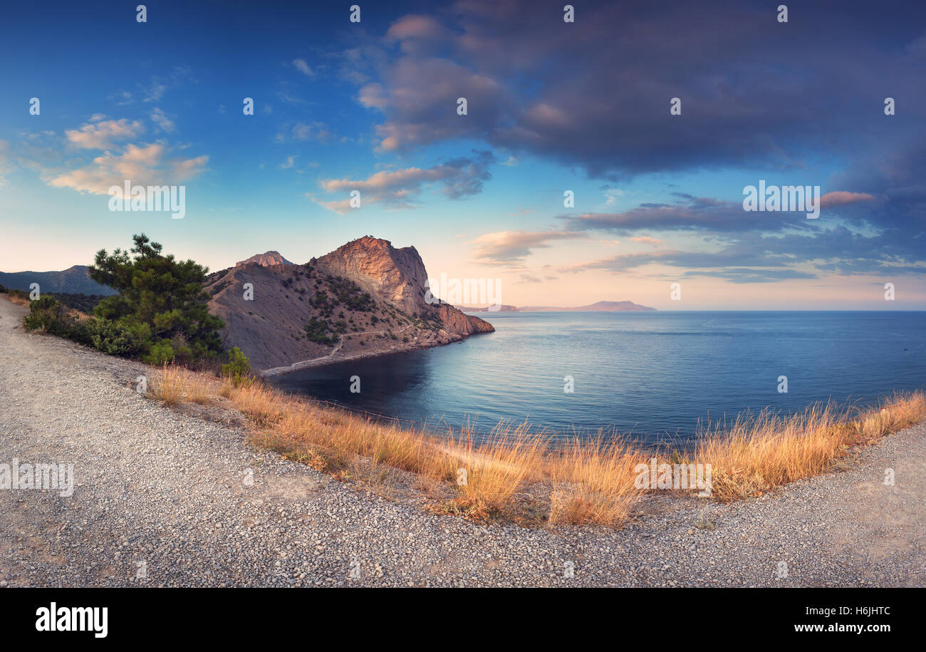 Colorido paisaje de montaña con PATH, hierba amarilla, el mar, el cielo azul y bellas nubes al atardecer en la Crimea. Verano en las montañas Foto de stock