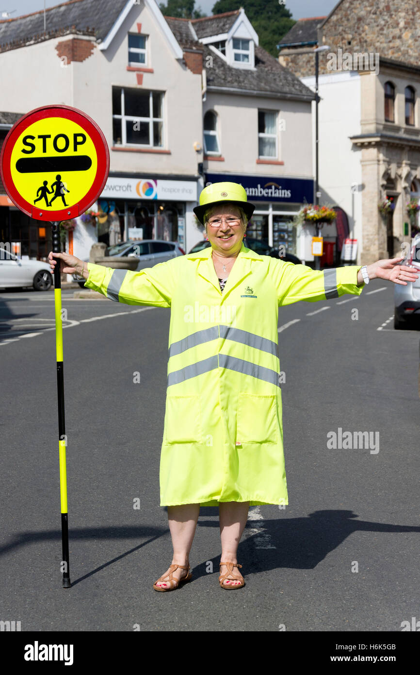 Lollipop lady (cruce de la escuela oficial de patrulla) detener el tráfico en Fore Street, Bovey Tracey, Devon, Inglaterra, Reino Unido Foto de stock