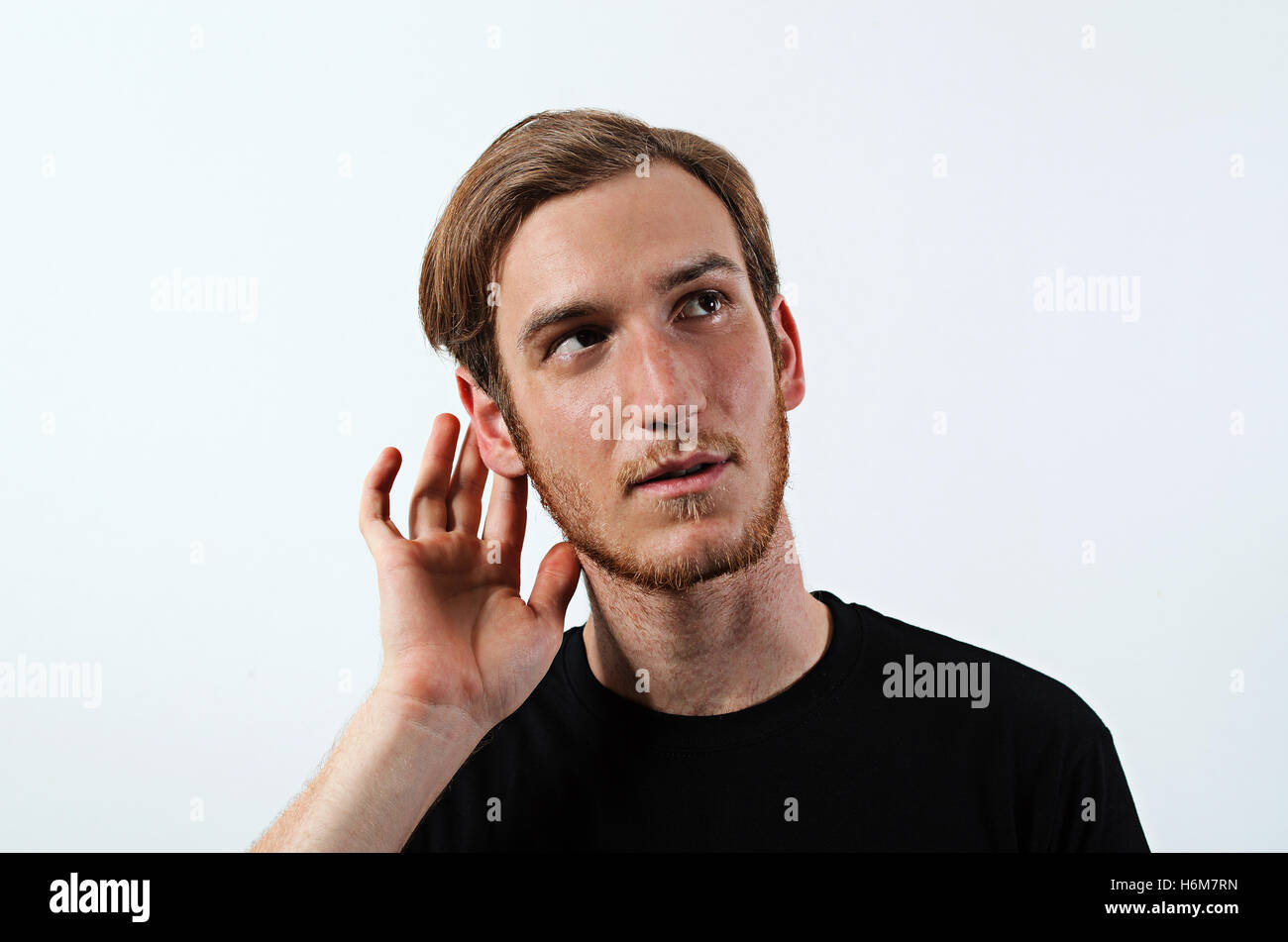 Un joven adulto macho oscuro vistiendo la camiseta con su mano cerca de su oído, joven adulto macho Foto de stock