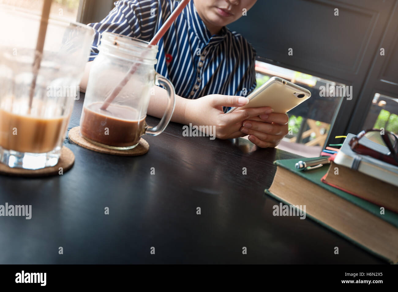 Mañana en el estilo de vida de la joven escena hipster mujer utilice el teléfono móvil mientras está sentado en la cafetería con libros y taza de café en la mesa. Tren Foto de stock