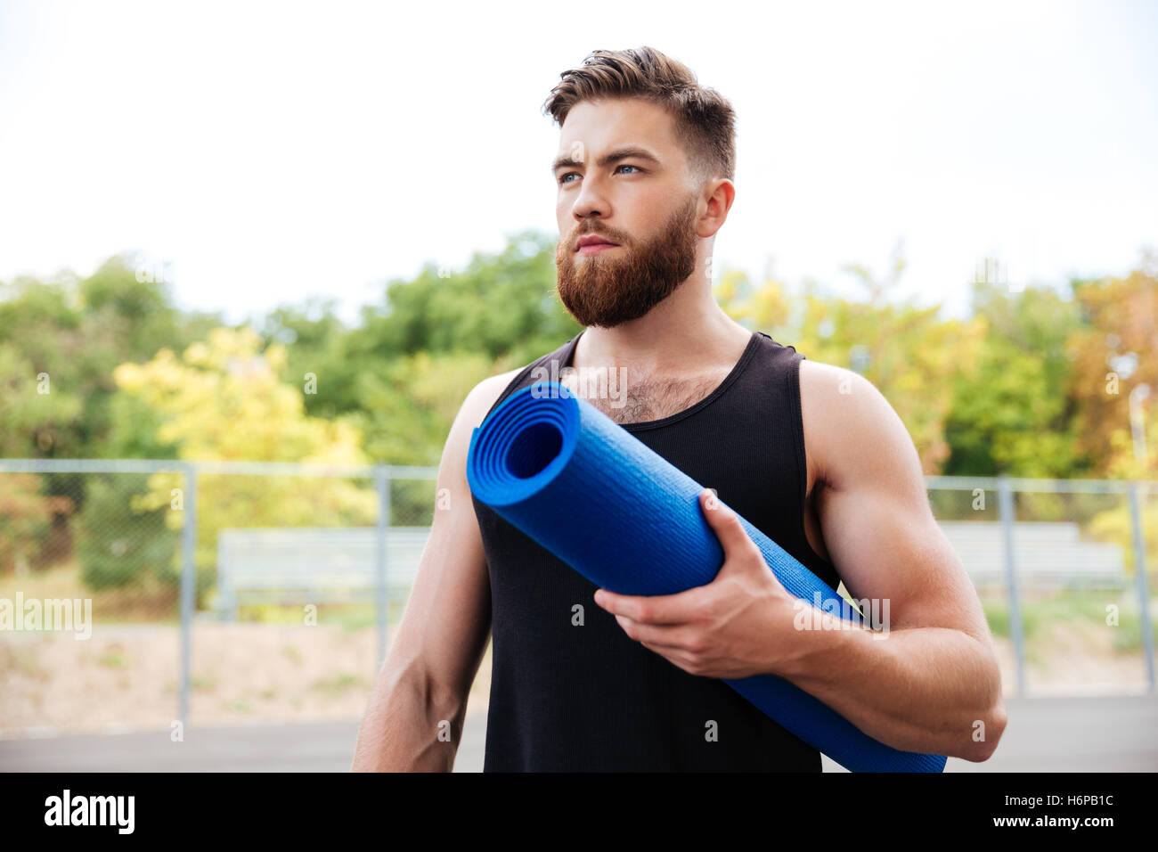 Instructor de yoga masculina graves concentrada la celebración de mat mientras está parado afuera Foto de stock