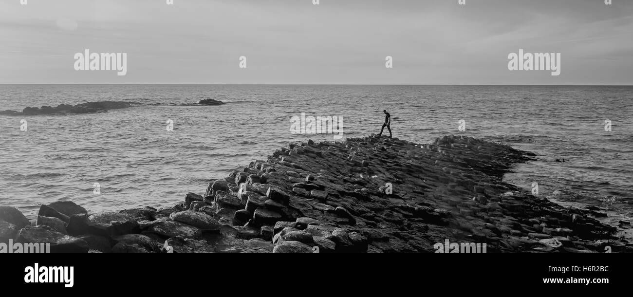 Una solitaria figura en la contemplación en el borde de la Calzada del Gigante en Irlanda, una tarde de verano, mirando al mar Foto de stock