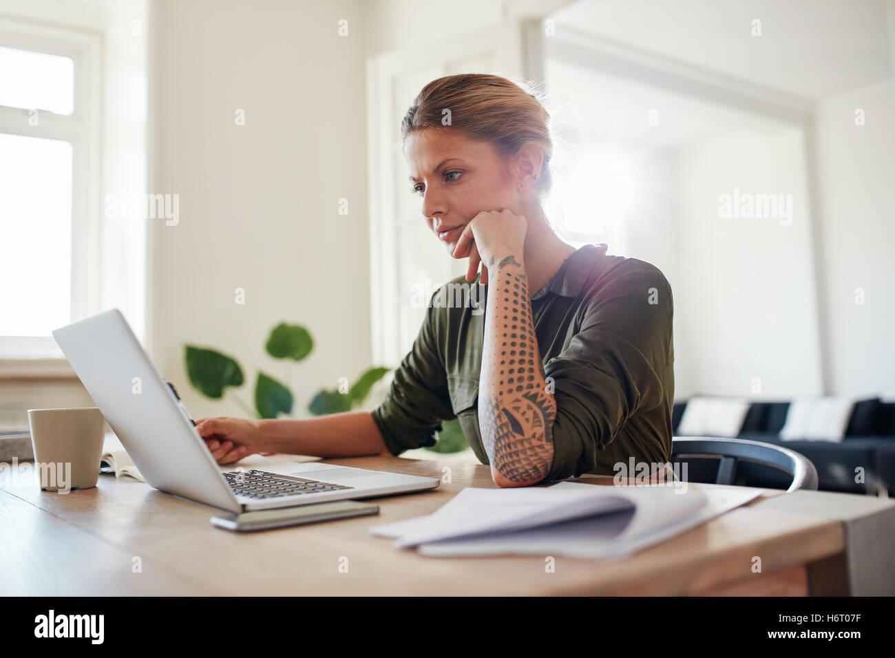 Filmación en interiores de joven mirando portátil en serio. Mujer sentada en la oficina en casa y el trabajo en equipo portátil. Foto de stock