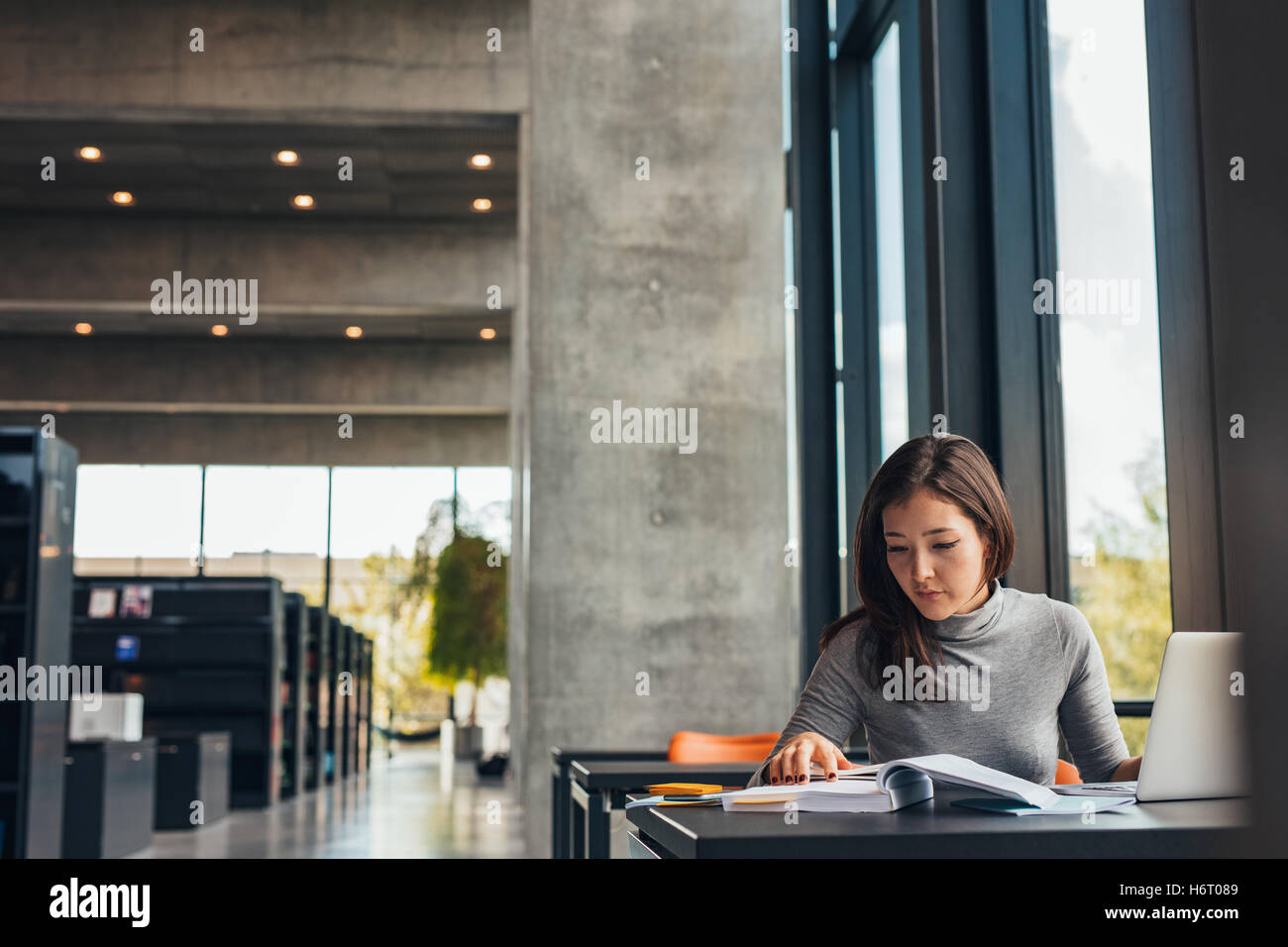 Filmación en interiores de joven estudiante hacer asignaciones en la biblioteca. Mujer Asiática leyendo libros de texto mientras está sentado en la biblioteca de la universidad. Foto de stock