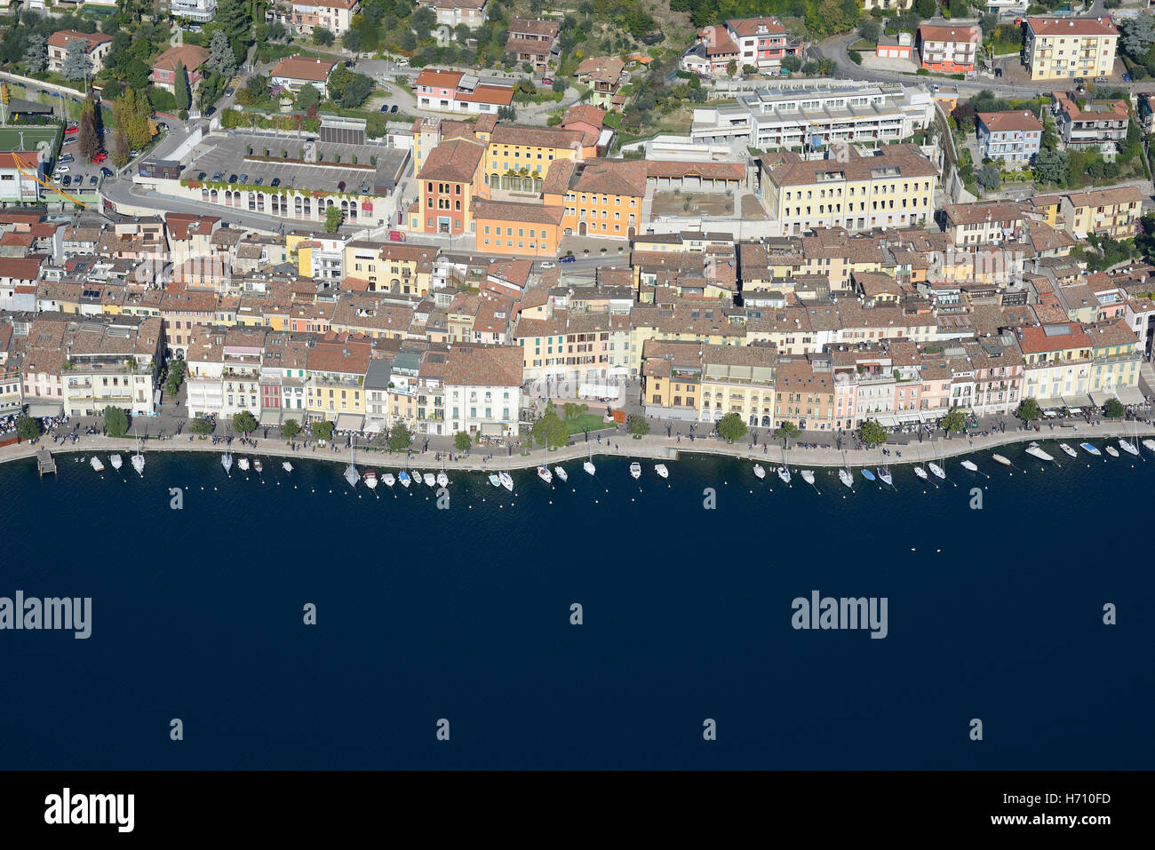 VISTA AÉREA. Pintoresca ciudad con su fila de barcos en la orilla del lago de Garda. Salò, Provincia de Brescia, Lombardía, Italia. Foto de stock
