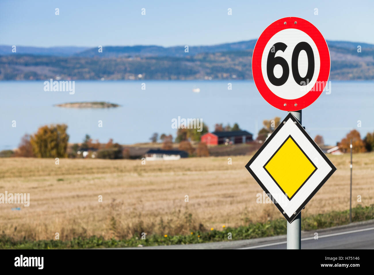 Carretera principal roadsign amarillo con señal de carretera de límite de velocidad montado en un poste de metal cerca de la carretera de Noruega rural Foto de stock