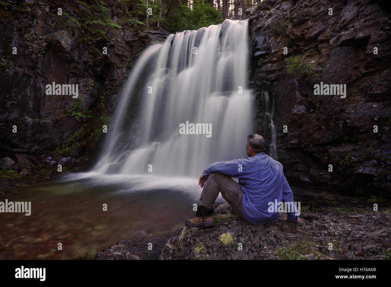 Hombre sentado junto a las cataratas Rockwell, Parque Nacional Glacier, Montana, Estados Unidos Foto de stock