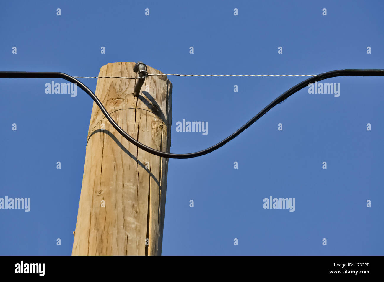 Primer plano de un cable eléctrico peligroso en un pilón de madera y el cielo claro Foto de stock