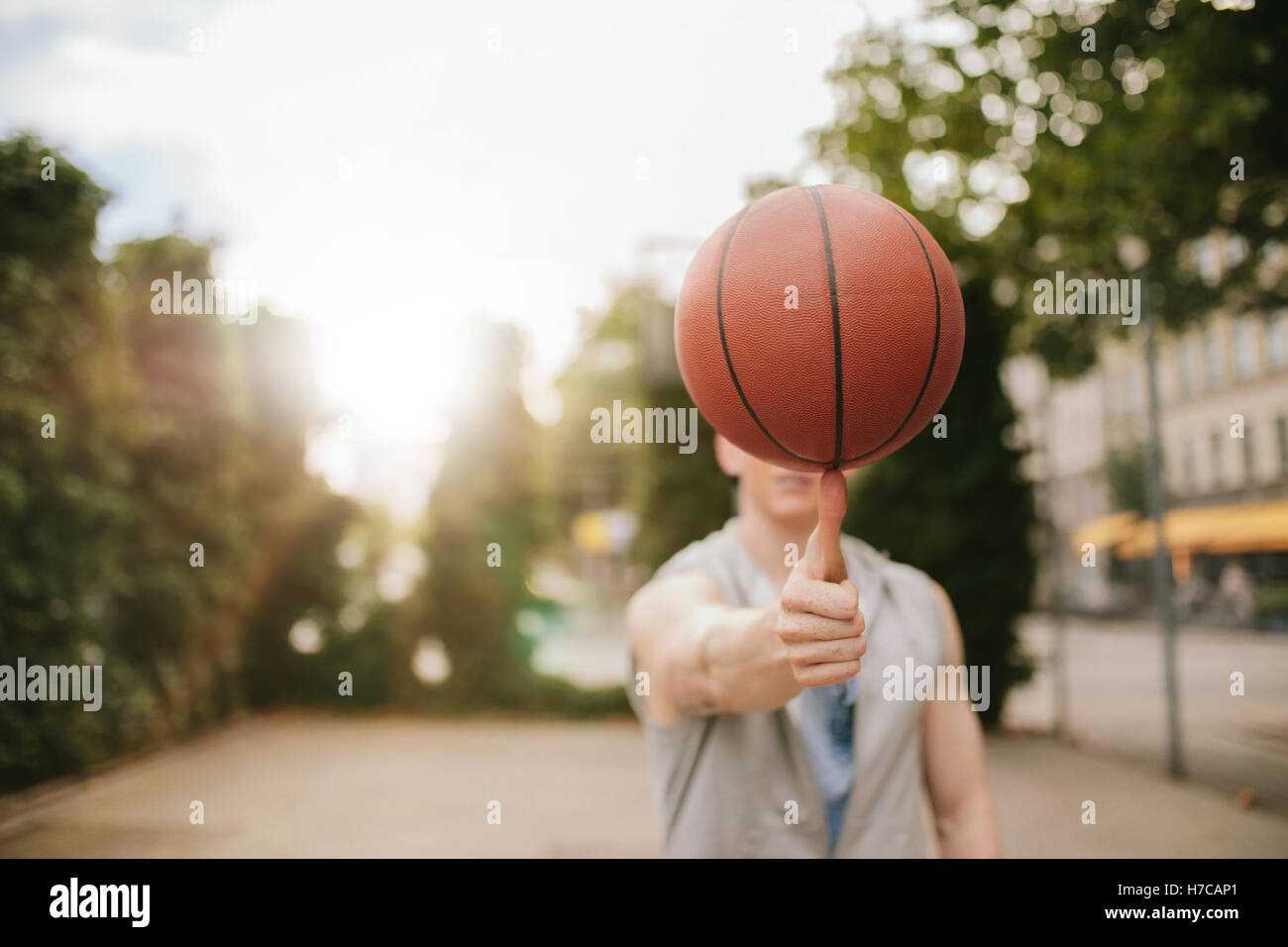Hombre Baloncesto equilibrado sobre su pulgar en el tribunal exterior. Jugador de Streetball gira la bola. Centrarse en el baloncesto. Foto de stock