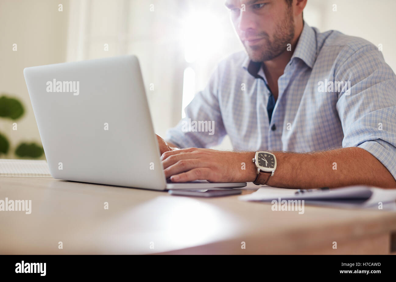 Foto de hombre joven sentado en la mesa y utilizando el portátil. Hombre de negocios caucásico trabajando desde casa. Foto de stock