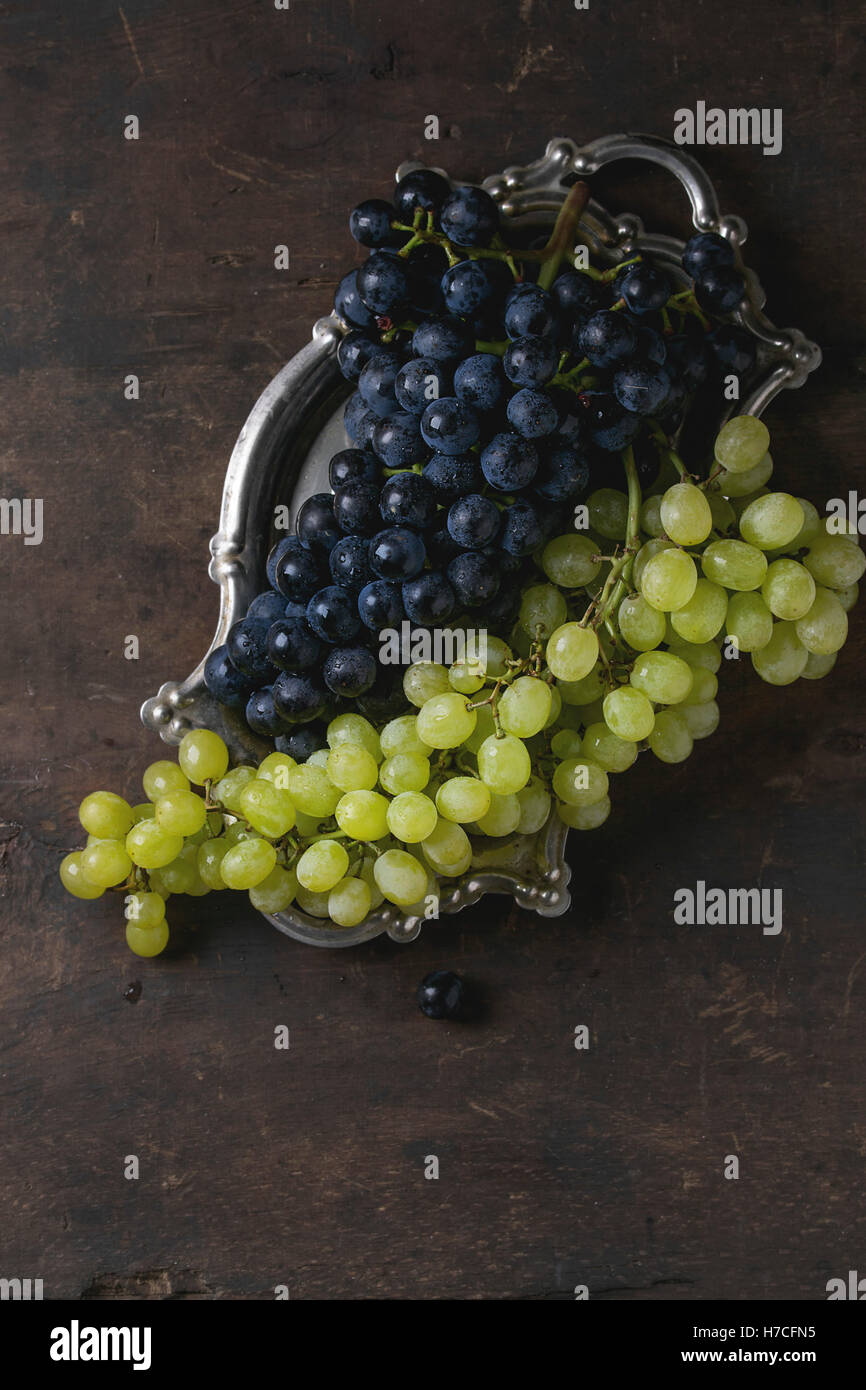 Húmedos maduros racimos de uvas rojas y blancas en vintage bandeja de