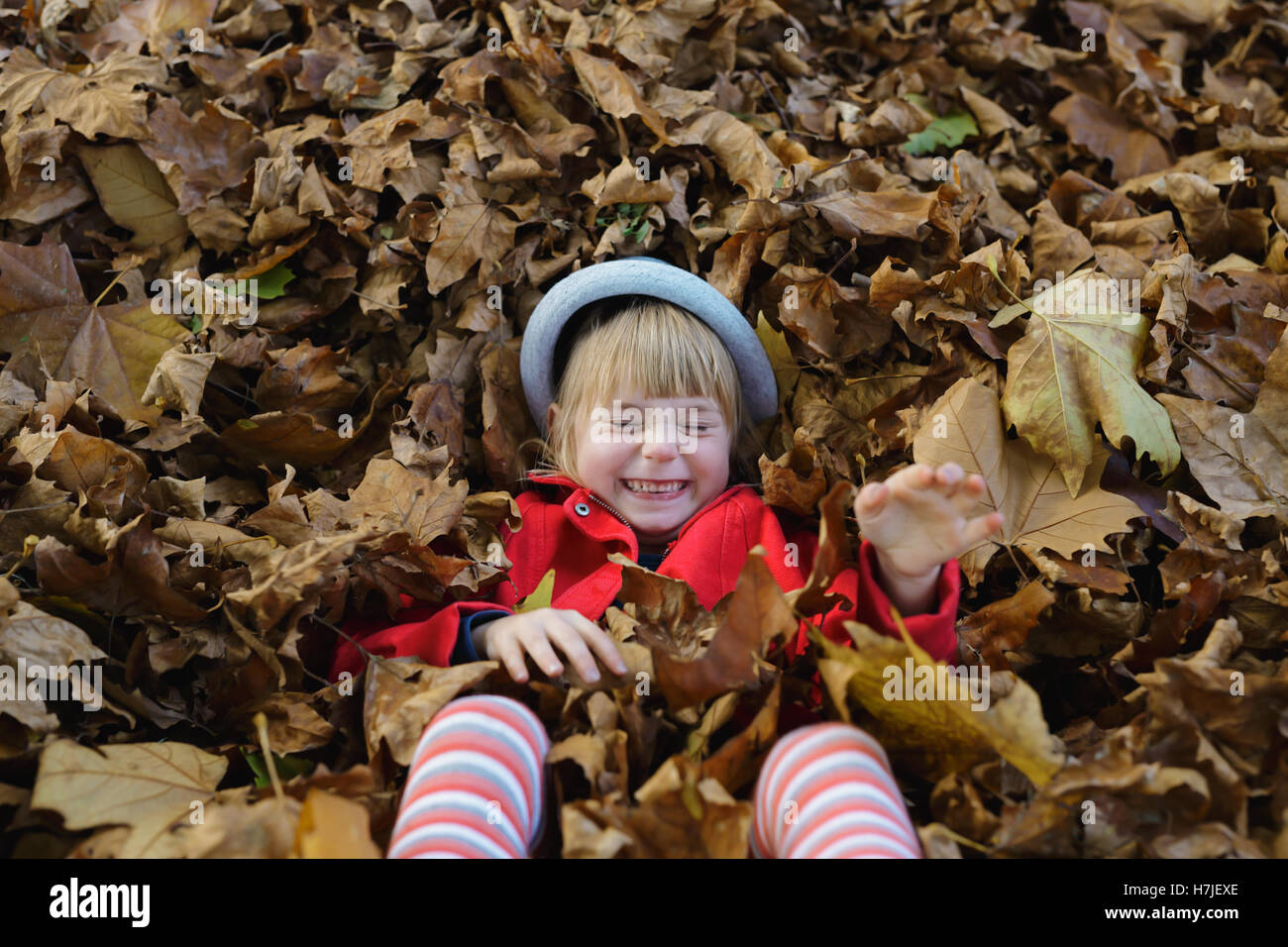 Feliz otoño. Niña chaqueta roja jugando con la pila de hojas secas en otoño del parque. Foto de stock