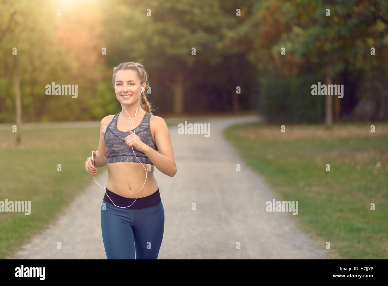 Mujer escuchando música en su reproductor de MP3 y tapones de oídos mientras correr por una carretera rural en un concepto de estilo de vida saludable Foto de stock