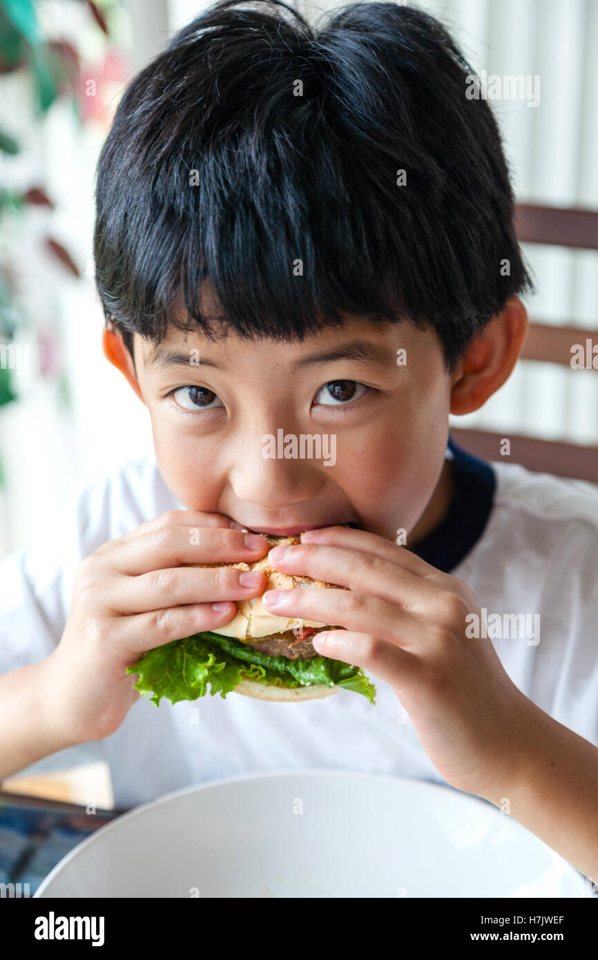 Chico asiático tomando un bocado a su hamburguesa. Foto de stock