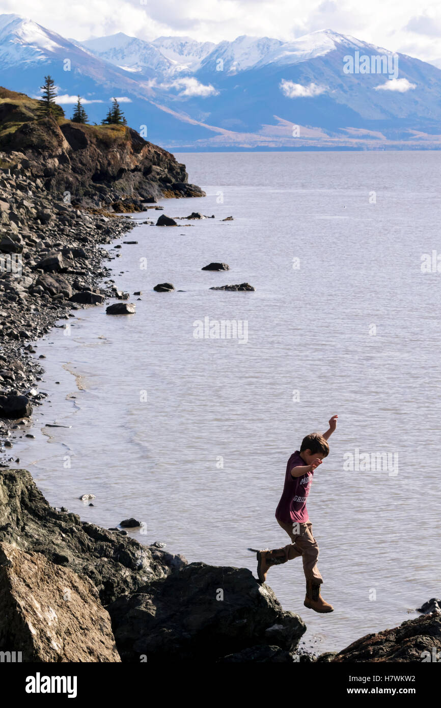 Joven saltando sobre rocas a lo largo del brazo Turnagain en verano, Southcentral Alaska, EE.UU. Foto de stock