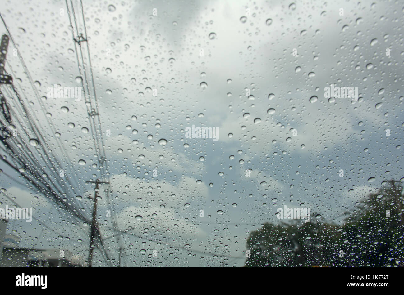 La lluvia caída en el coche de cristal con poste eléctrico y nubes en el cielo Foto de stock