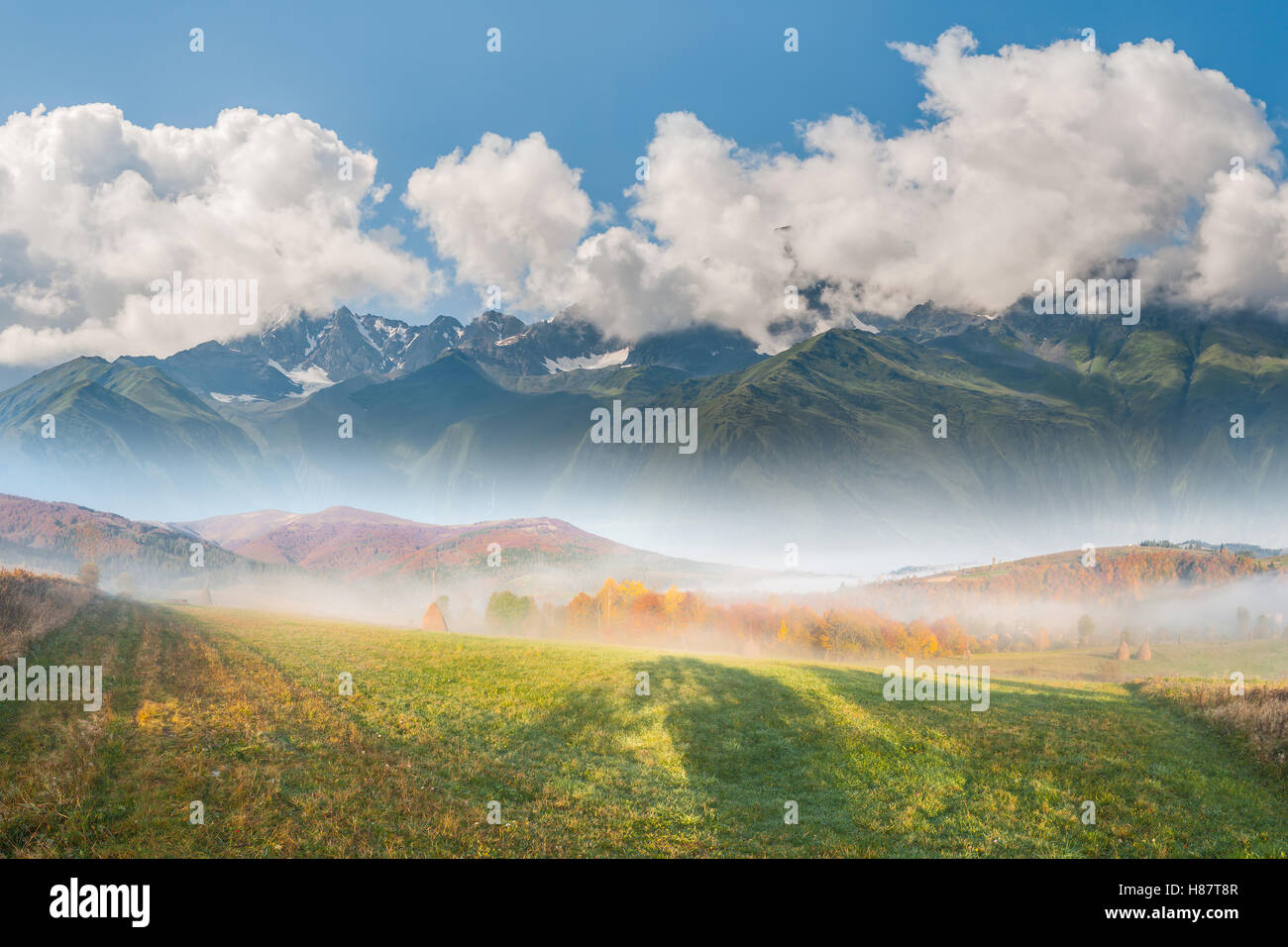 Hermoso paisaje con pradera, montaña, niebla y nubes Foto de stock