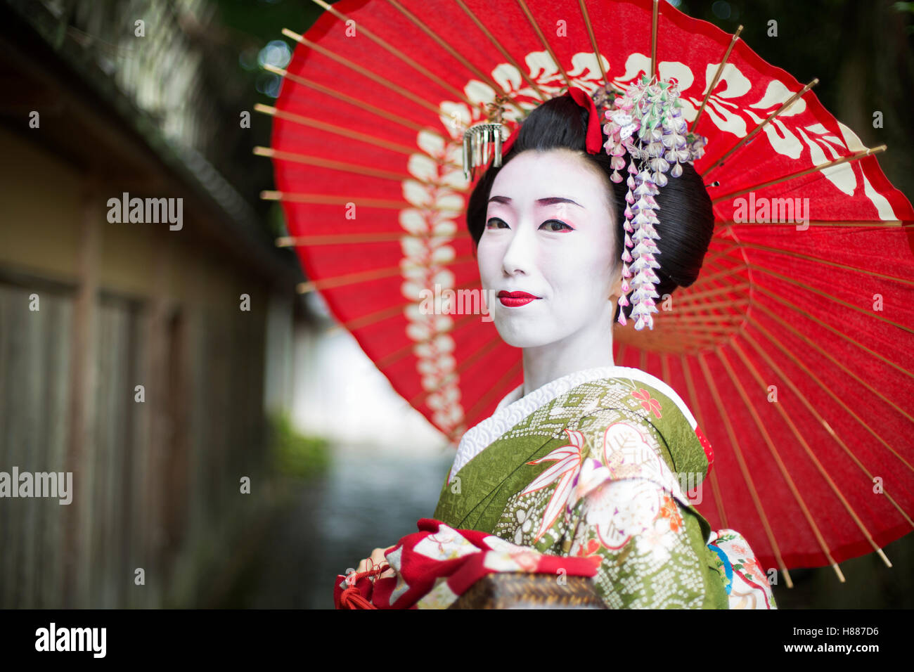 Una mujer vestida con el tradicional estilo geisha, vistiendo un kimono y  obi, sosteniendo una sombrilla de papel rojo Fotografía de stock - Alamy