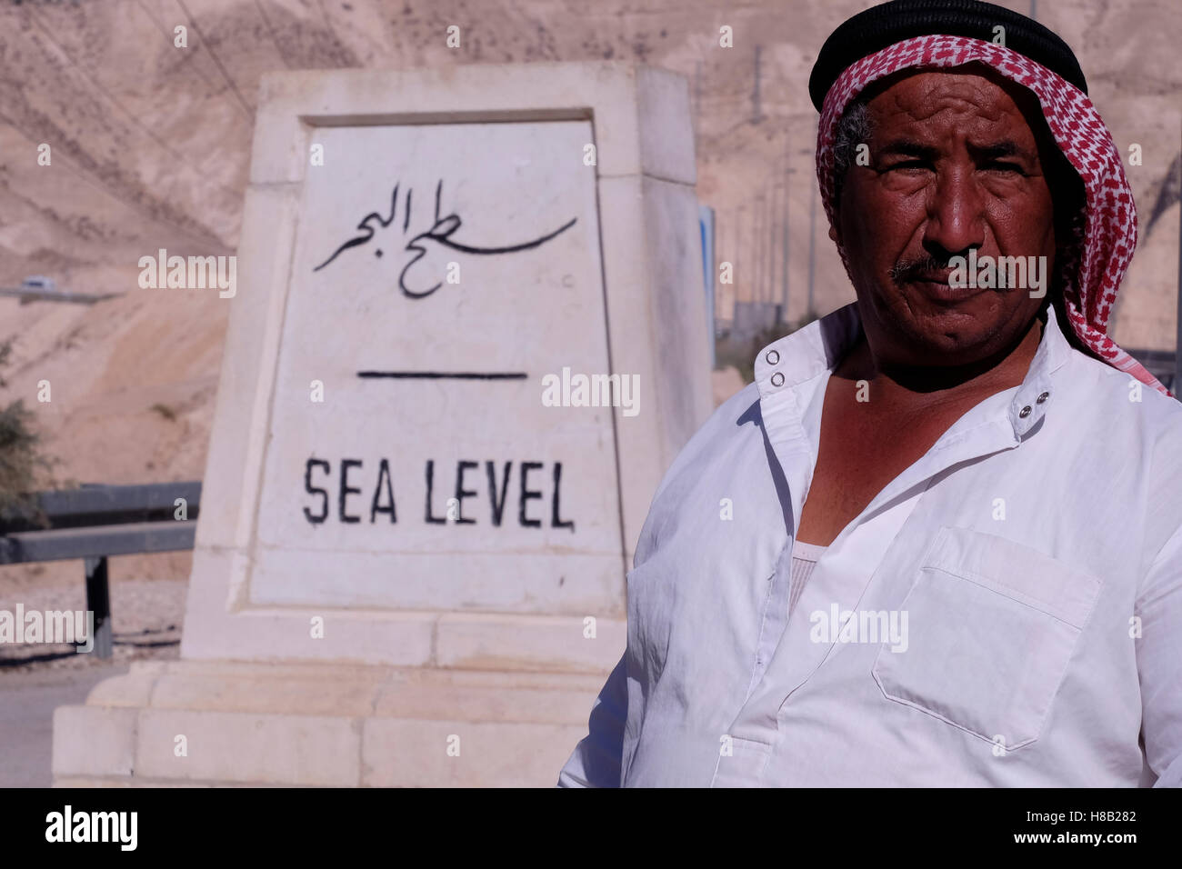 Un hombre palestino posando junto a un indicador de nivel del mar, en la carretera de Jerusalén hasta el Mar Muerto en el desierto de Judea o de Judea Israel Foto de stock