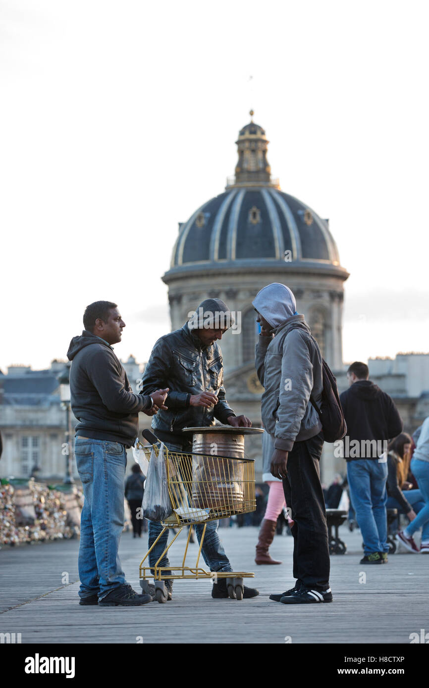 Los inmigrantes que venden los castaños de Indias asado en Pont des Art, dominada por la cúpula del Institut de France, París, Francia Foto de stock