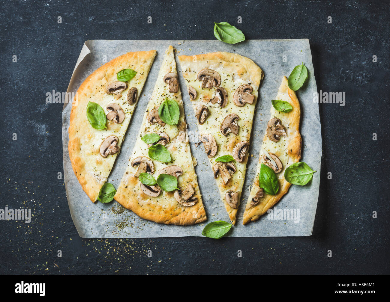 Champiñón pizza casera con albahaca cortada en rebanadas sobre papel para  hornear sobre fondo de piedra negra, vista superior, composición horizontal  Fotografía de stock - Alamy