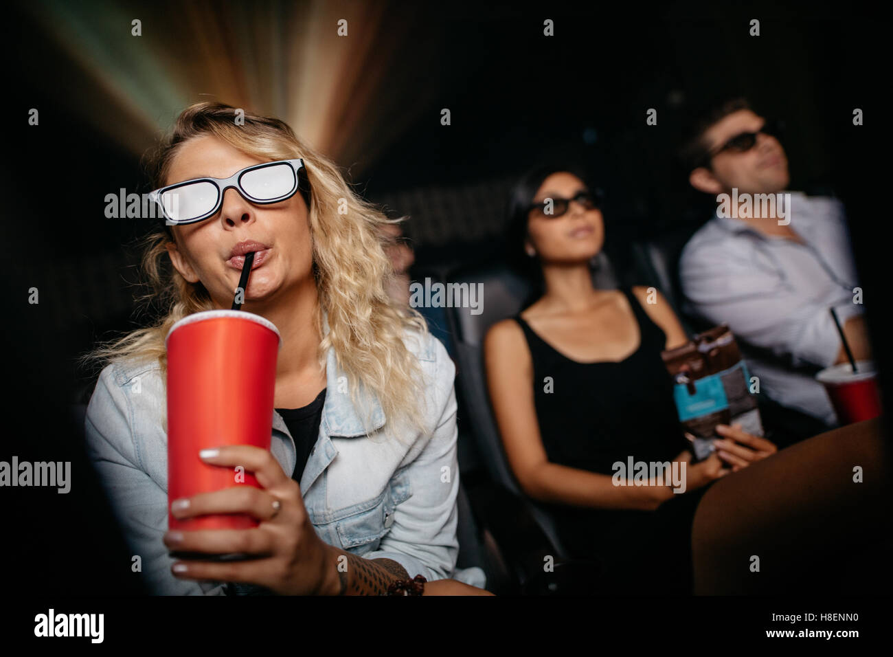 Mujer joven tener bebida fría llevar gafas 3D y ver la película en el teatro. La gente en el cine viendo la película en 3d. Foto de stock