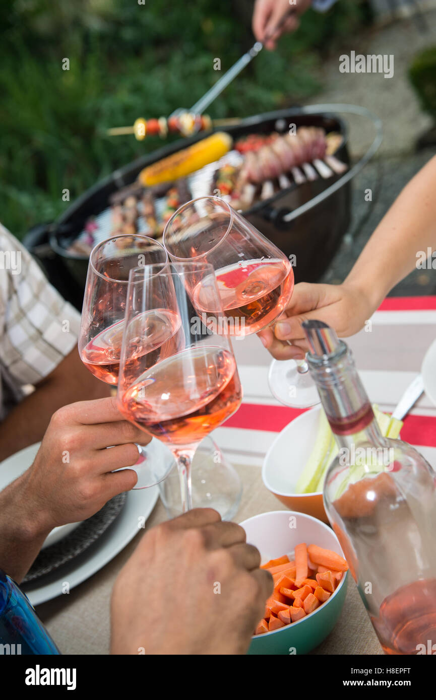 Feliz amigos divertirse al aire libre, centrándose en manos de vidrio de vino rosado de tostado durante la barbacoa Foto de stock