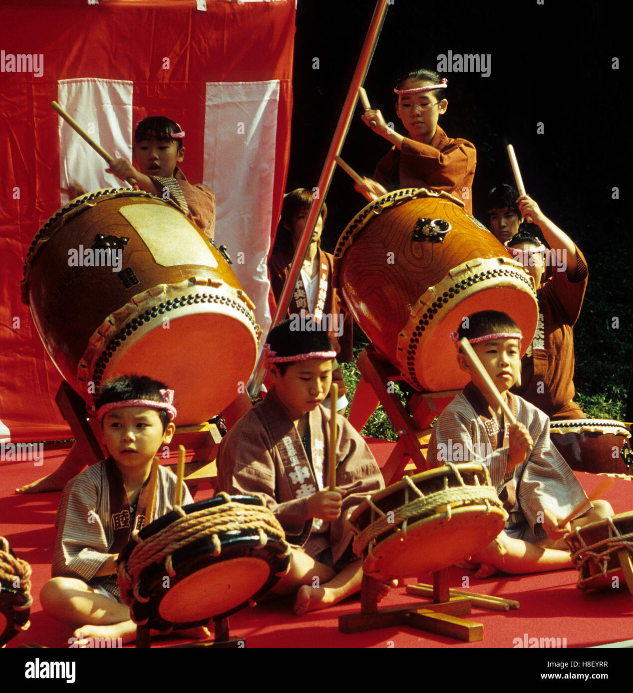 Los niños japoneses tocando tambores tradicionales para el festival