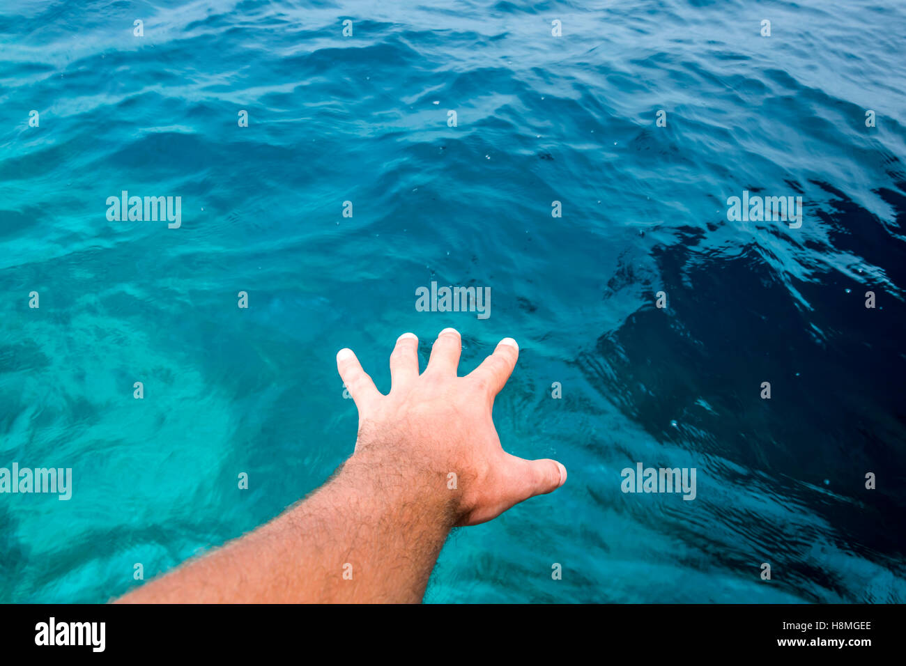 Mano de un joven varón caucásico apareciendo a tocar la superficie de increíbles aguas azules del Océano Índico. Foto de stock