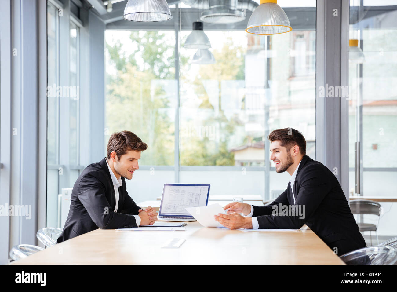 Dos jóvenes empresarios feliz trabajando juntos usando portátil en reunión de negocios en la oficina Foto de stock