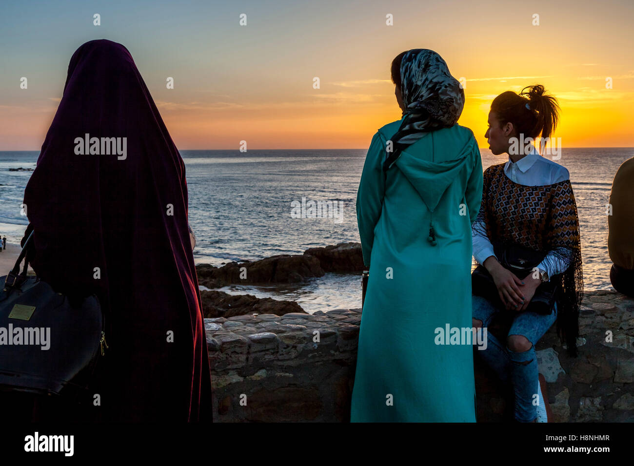La gente joven marroquí ver el atardecer desde un punto de vista popular en la localidad costera de Asilah, Marruecos Foto de stock