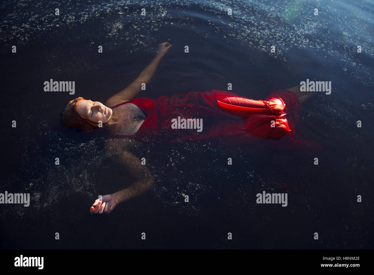 Mujer de vestido rojo flotando sobre el agua Foto de stock