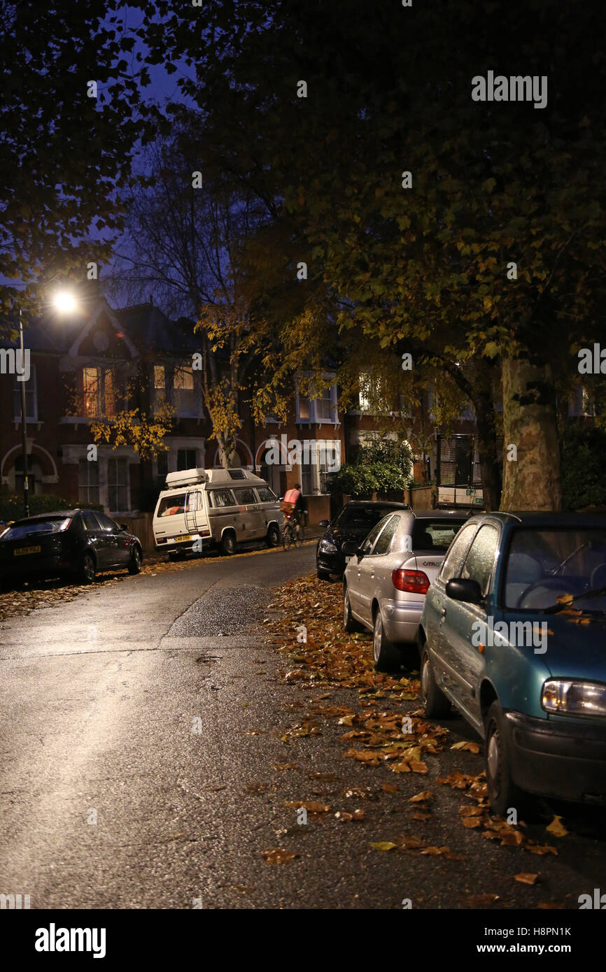Hojas de otoño cubren las aceras y calles en una típica calle de Londres del sur tras la oscuridad en una noche húmeda Foto de stock