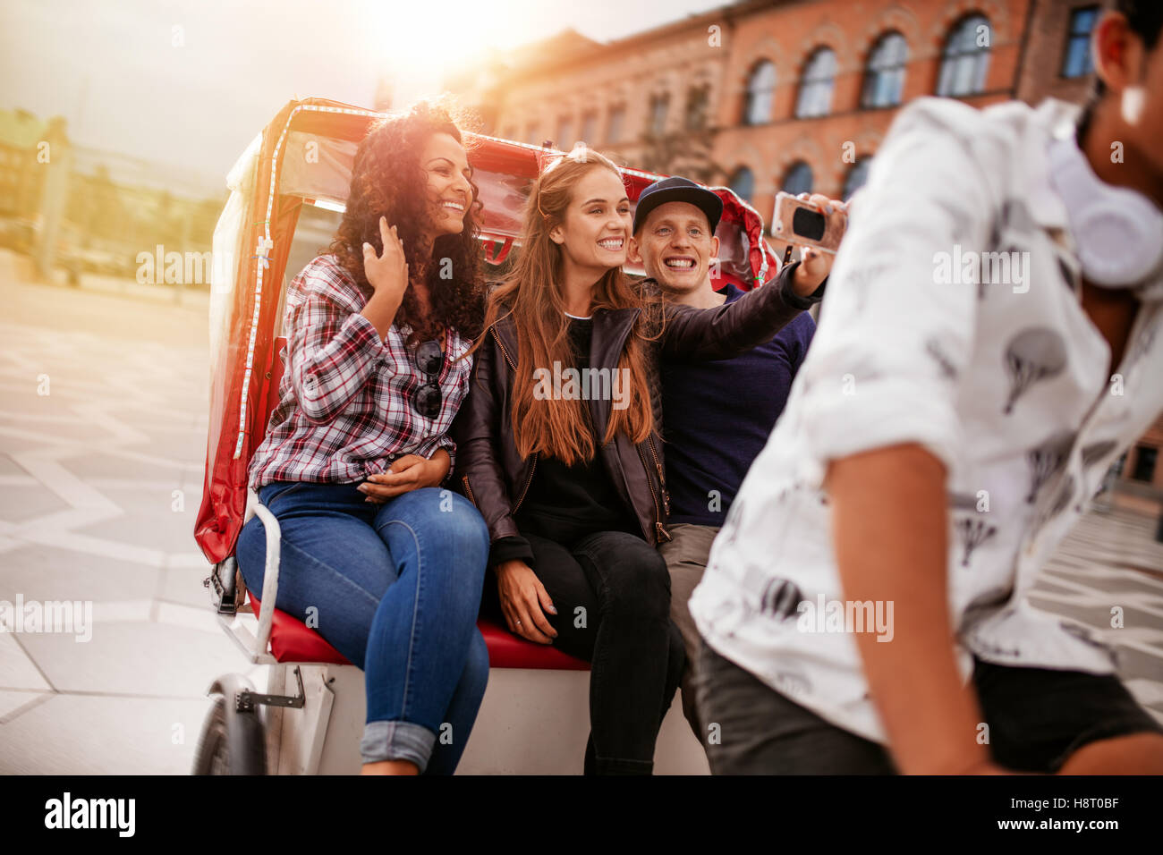 Jóvenes amigos tomando selfie en triciclo de paseo. Las mujeres jóvenes y el hombre a caballo en triciclo bicicleta y tomar autorretratos. Foto de stock