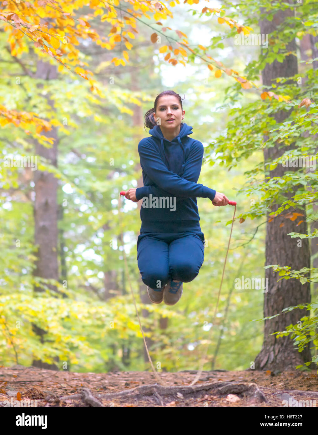 Hermosa joven mujer fitness comba en bosque, colores de otoño Foto de stock