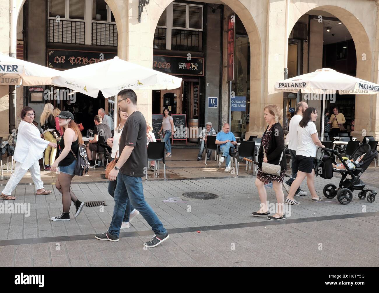 Peatones a lo largo de C. Portales en la Plaza del Mercado en Logroño, España pasan La Taberna de Portales con sus asientos al aire libre en verano. Foto de stock