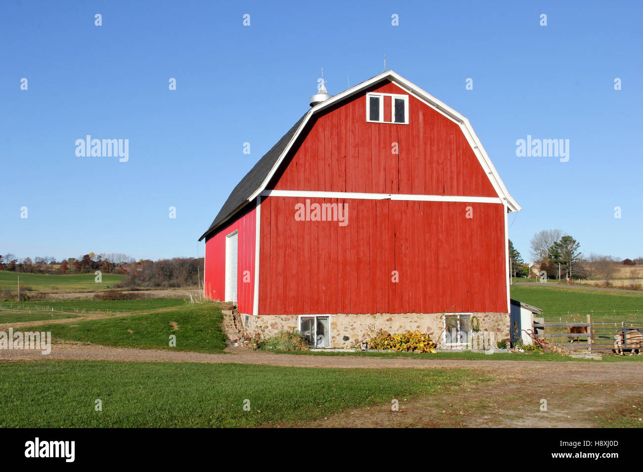 Granja de madera roja en una granja de Wisconsin con hierba verde y azul cielo de fondo Foto de stock