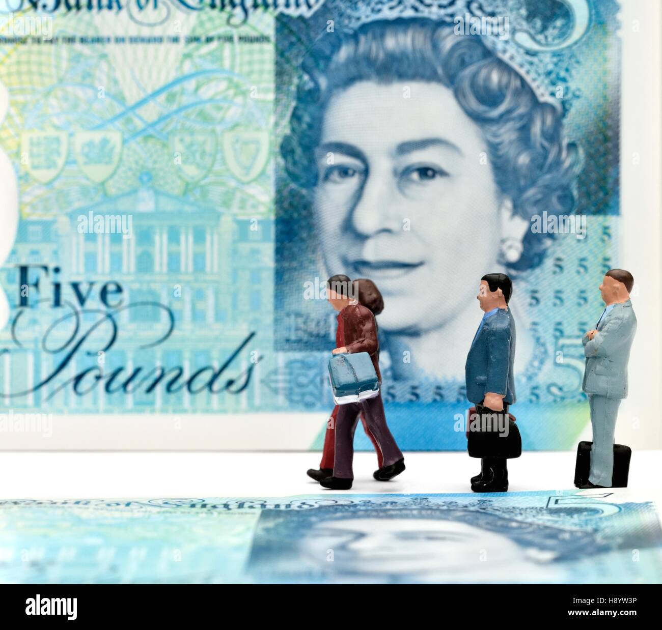 Figuras en miniatura caminando delante de una nota de cinco libras. Foto de stock
