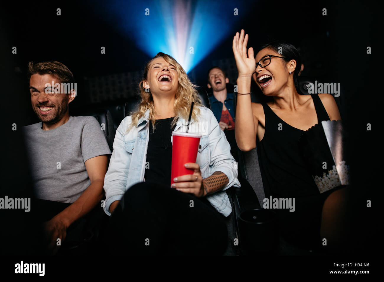 Grupo de personas en cine con palomitas y bebidas viendo la película y riendo. Mujeres y hombres jóvenes viendo la película de comedia en el cine. Foto de stock