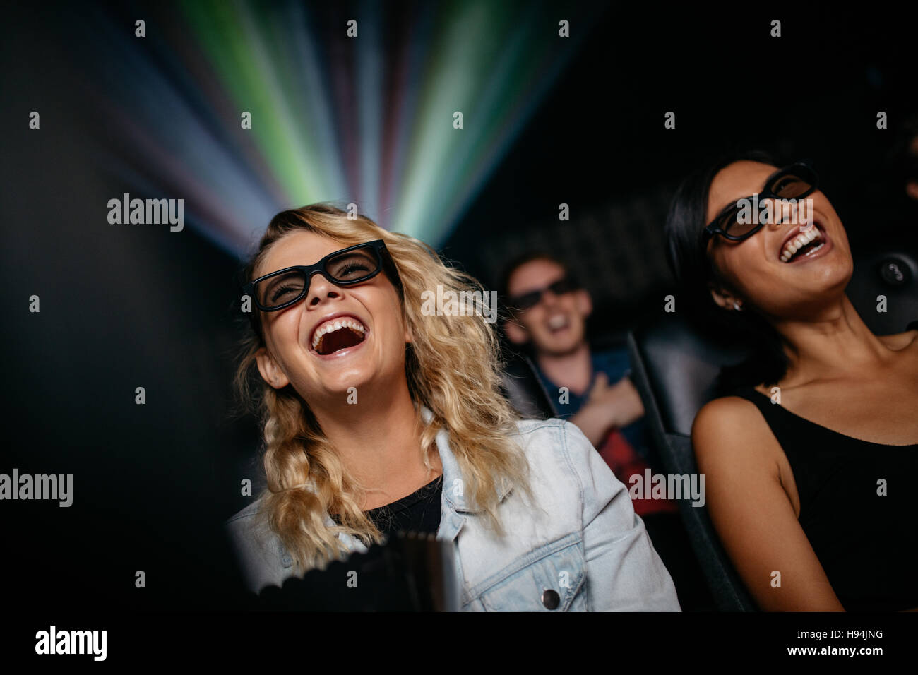 Mujer sonriente amigos viendo películas en 3D en el teatro. Las mujeres jóvenes felices viendo películas en 3D en un multicine. Foto de stock